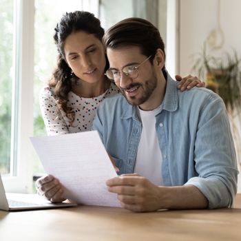 A mom and dad review a bank statement at a dining table.