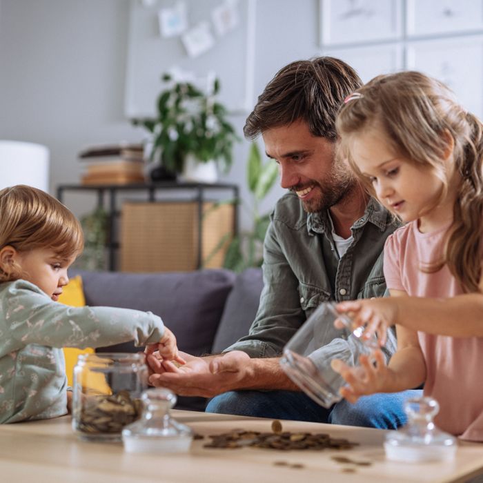 A father smiles as a preschooler and her younger brother count pennies from their money jars.