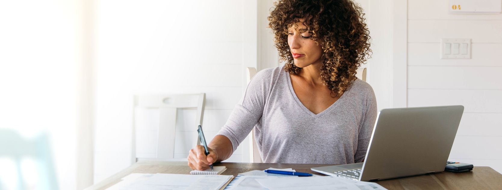 A woman jots down some notes next to her laptap.